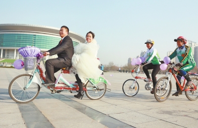 氣球和鮮花裝點(diǎn)的雙人自行車，新郎郝幸福載著美麗新娘回家。