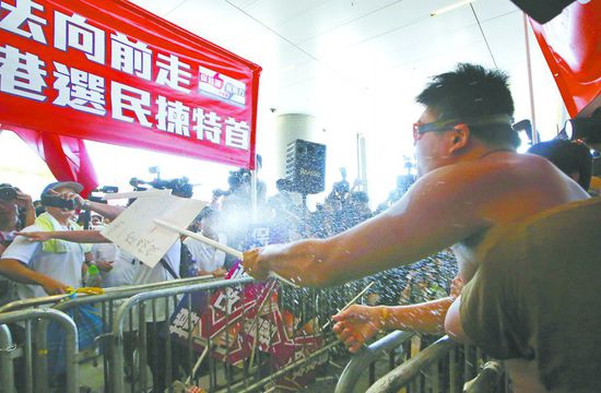 17日，在香港立法會外，一名反對政改的男子向支持派人群投擲標牌。