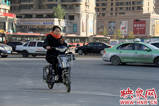 一名女士騎著電瓶車看著手機(jī)