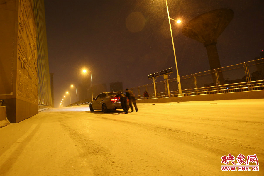 雪天路滑，汽車上橋打滑，兩名“推車人”幫助一輛私家車上坡。