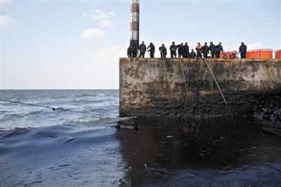 昨日，山東青島，清污人員正在海邊清理油污。