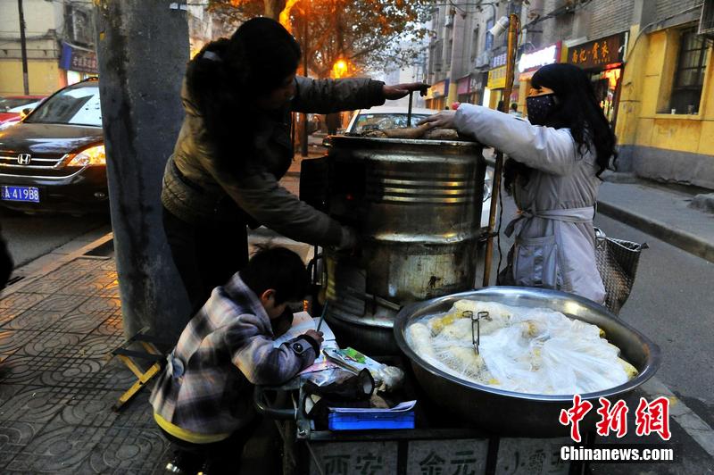 男孩西安路燈下寫作業(yè) 媽媽邊賣紅薯邊輔導(dǎo)